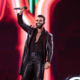 Cantor sertanejo no palco com microfone erguido e iluminação neon no Pinda Rodeio Fest 2026 — foto divulgação