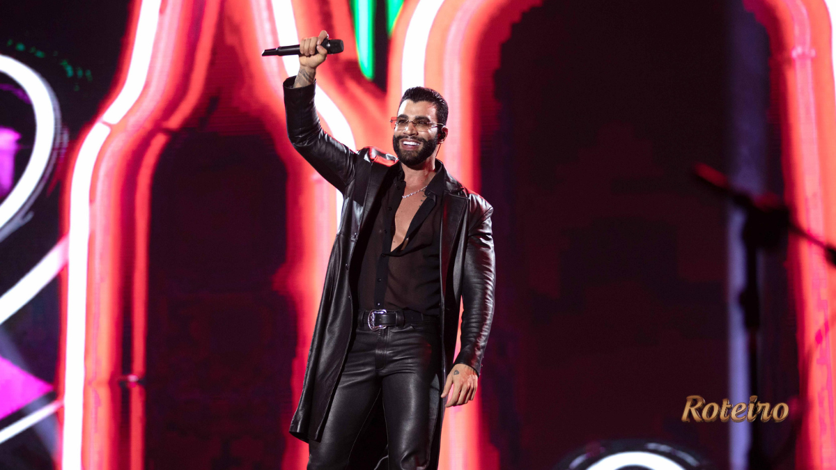Cantor sertanejo no palco com microfone erguido e iluminação neon no Pinda Rodeio Fest 2026 — foto divulgação