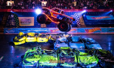Monster truck com design em chamas e número 68 realiza salto espetacular sobre carros amassados durante o espetáculo Hot Wheels Monster Trucks Live Glow n' Fire, com arena lotada e iluminação neon ao fundo. Foto: Divulgação/Hot Wheels