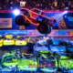 Monster truck com design em chamas e número 68 realiza salto espetacular sobre carros amassados durante o espetáculo Hot Wheels Monster Trucks Live Glow n' Fire, com arena lotada e iluminação neon ao fundo. Foto: Divulgação/Hot Wheels
