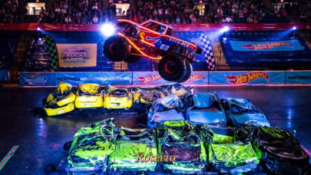 Monster truck com design em chamas e número 68 realiza salto espetacular sobre carros amassados durante o espetáculo Hot Wheels Monster Trucks Live Glow n' Fire, com arena lotada e iluminação neon ao fundo. Foto: Divulgação/Hot Wheels