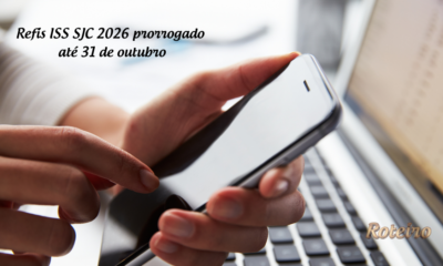 Refis ISS SJC 2026 prorrogado até 31 de outubro: mãos segurando celular em frente a notebook para adesão online
