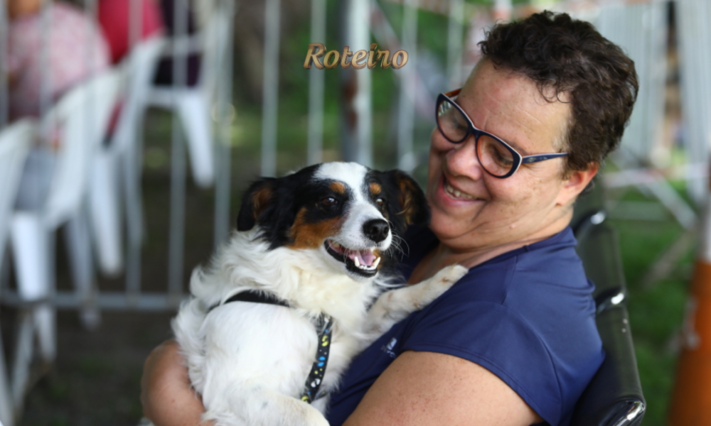 castração gratuita em SJC, tutora sorridente segura no colo cachorro preto, branco e caramelo
