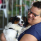 castração gratuita em SJC, tutora sorridente segura no colo cachorro preto, branco e caramelo