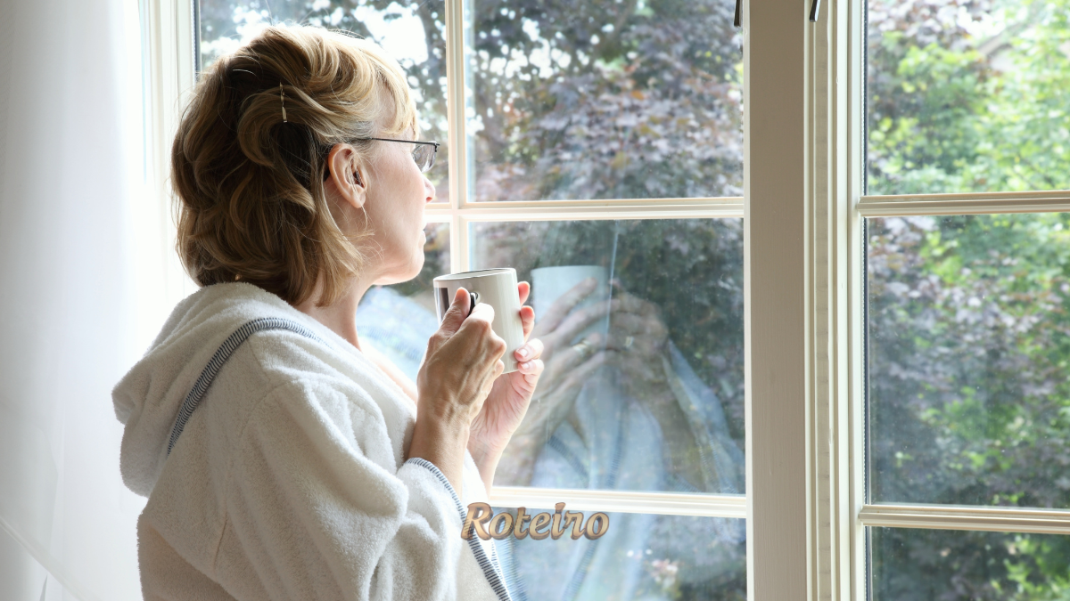 Como começar o autoconhecimento: mulher faz uma pausa e olha pela janela com uma xícara nas mãos