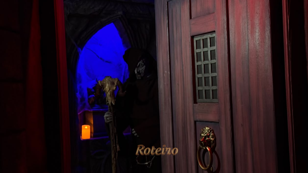 Halloween Castelo do Terror: personagem encapuzado com máscara de caveira e cajado surge atrás de porta de madeira no percurso da atração